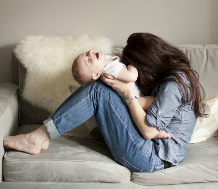 Chica sentada en un sofá haciéndole cosquillas a un bebé