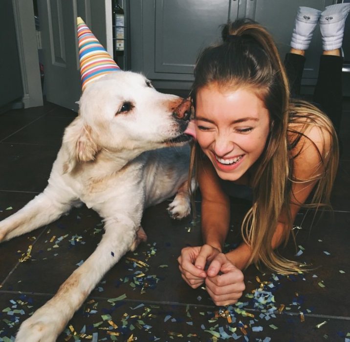 Chica sentada junto a un perro mientras la lame en la mejilla 