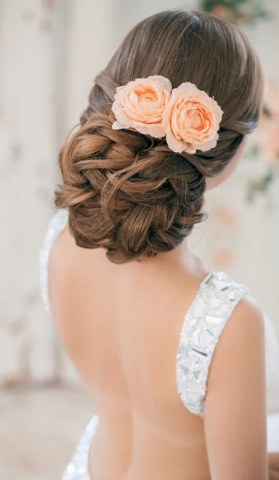 Peinados para el día de tu boda chica usando un chongo bajo con rosas color salmón como accesorio 