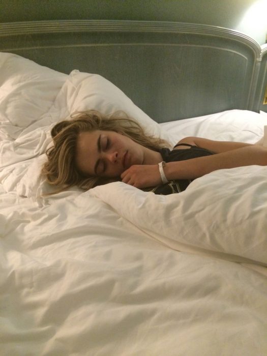 Cara Delevinge durmiendo sobre una cama blanca 