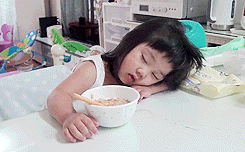 GIF Niña dormida sobre la mesa intentando comer un cereal 