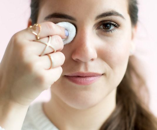 Chica sosteniendo un algodón con removedor de maquillaje sobre su ojo 