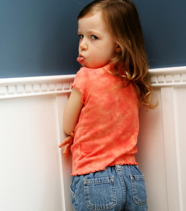 niña de pie en la esquina haciendo tiempo de castigo saca la lengua