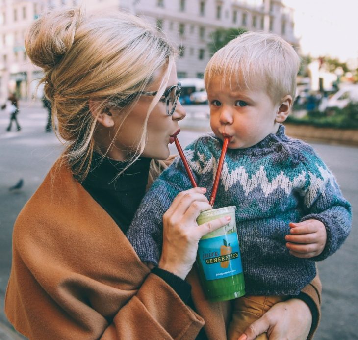 madre cargando hijo con vaso popote ciudad 