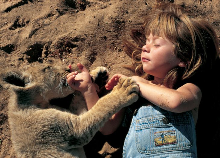 niña tippi en la arena abrazada de un leon cachorro