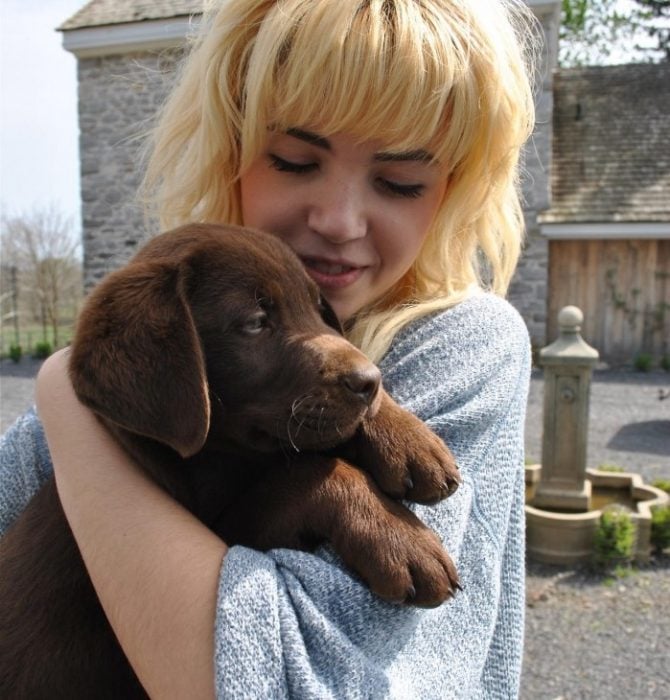 chica rubia abrazando a cachorro labrador cafe