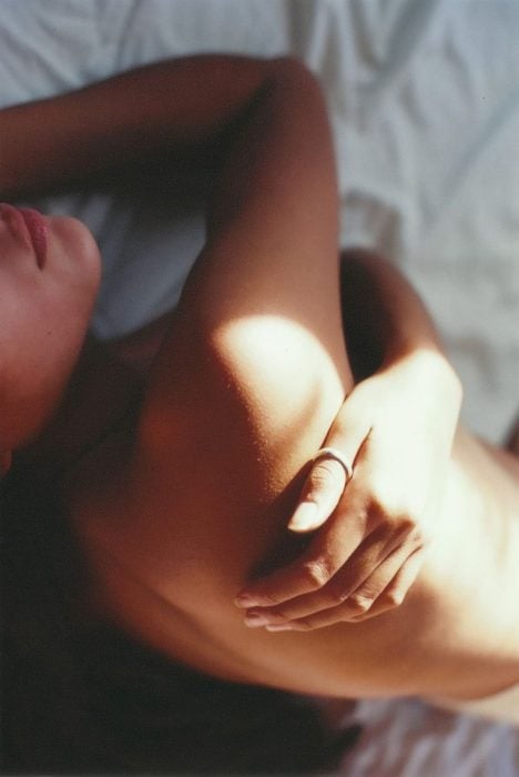 mujer desnuda se abraza asi misma en la cama rayo de sol 