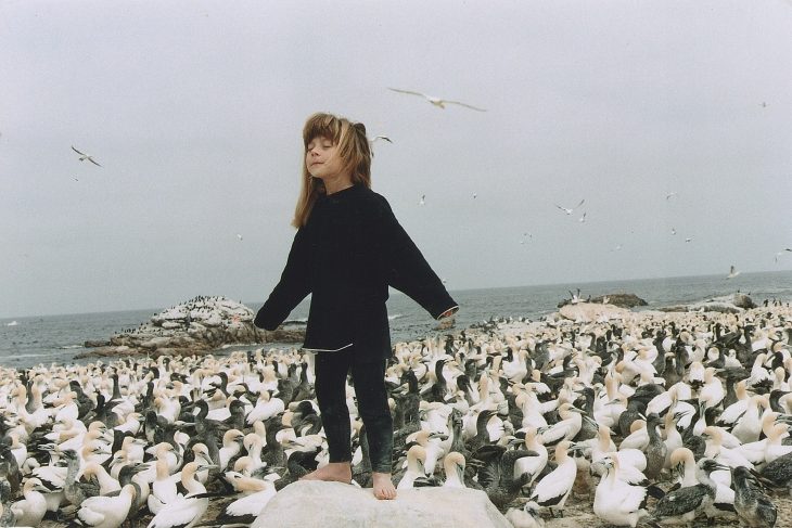 niña tippi de pie con ojos cerrados y gaviotas 