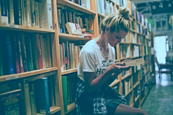mujer rubia en biblioteca leyendo 