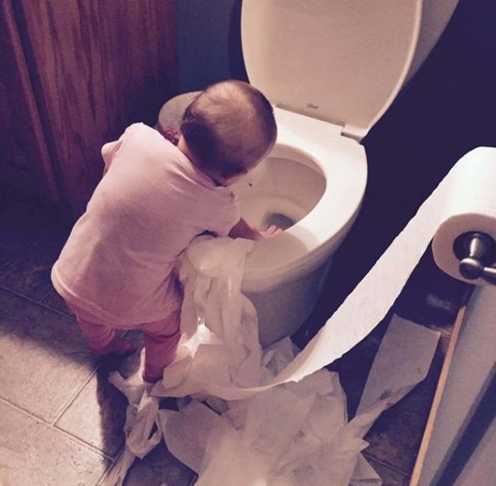 niña jugando con el papel de baño y el retrete 