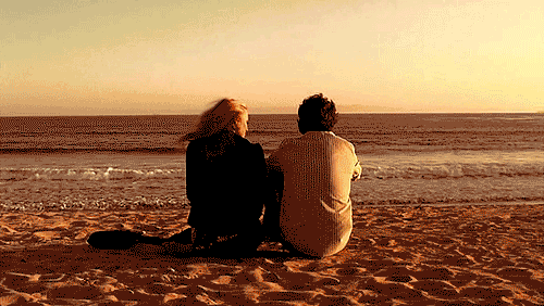 GIF pareja de novios sentados en la playa conversando 