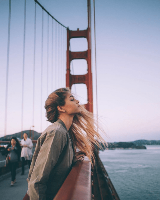 Chica recargada sobre un puente mientras disfruta el aire 