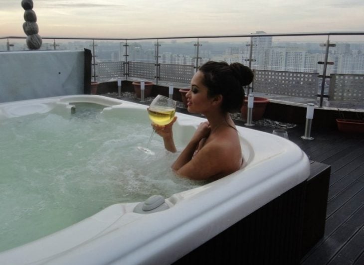 Chica tomando una copa de vino mientras toma un baño al aire libre