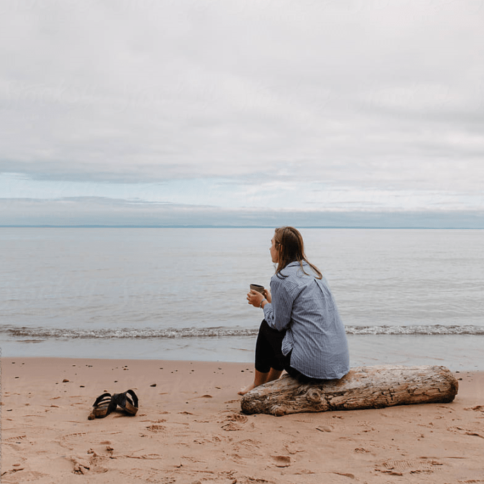 chica rubia sentada en la playa con una taza de café