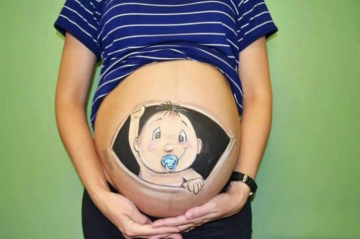 Pancita de una chica embarazada pintada con un niño que se está asomando desde la panza 