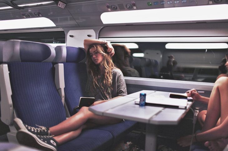 mujer sentada en asiento de tren leyendo libro con brazo en la mano