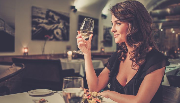 Chica sosteniendo una copa de vino mientras cena sola