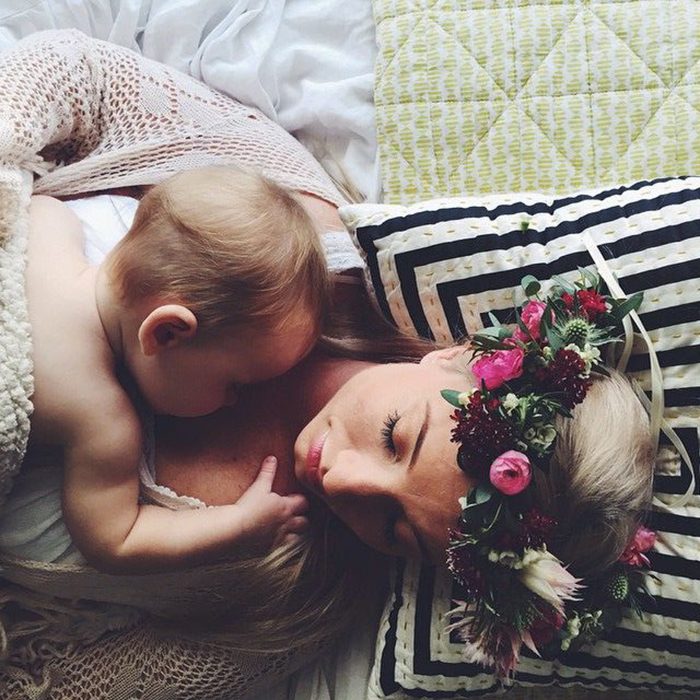 madre acostada con corona de flores y su bebé en el pecho 