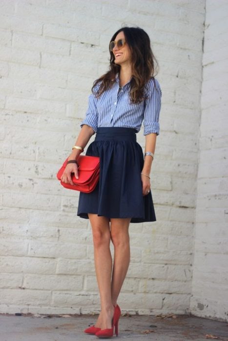 Chica usando una blusa azul con lineas verticales y una falda color azul marino, bolso y zapatos rojos