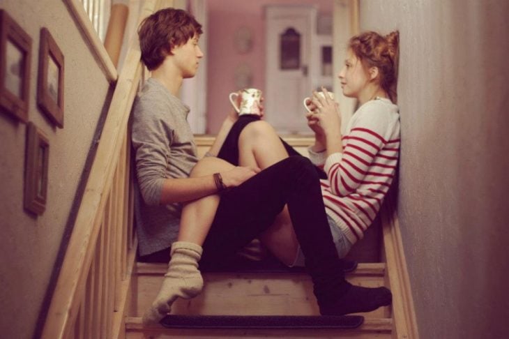 Chica y chico sentados en unas escaleras tomando café