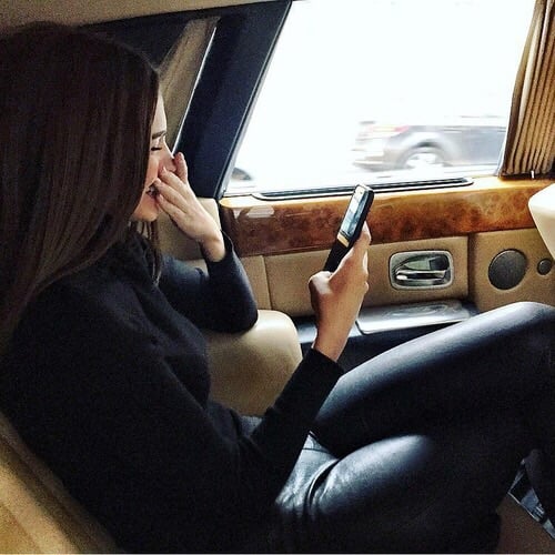 Chica sentada en el asiento trasero de un coche revisando su celular 