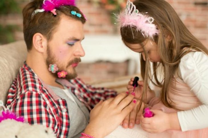 Padre jugando con su pequeña hija mientras le pinta las uñas de color rosa