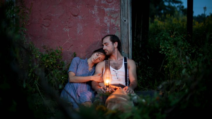 Pareja de novios sentados sobre el cesped sosteniendo una lámpara de lava 