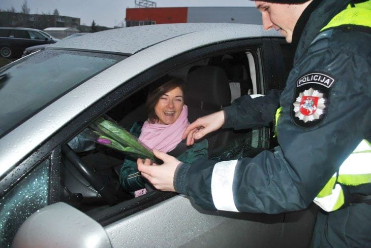 Policia entregando flores a una mujer que está conduciendo 