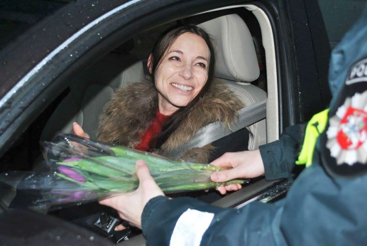 Policia entregando flores a una mujer que está conduciendo 