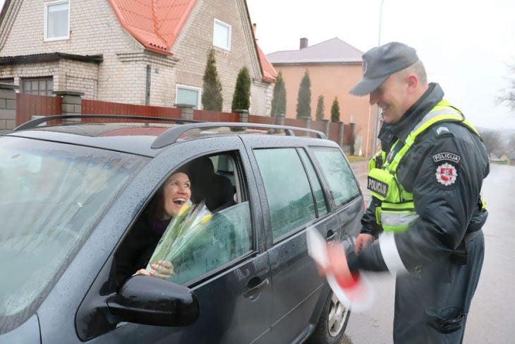Policía entregando flores a una mujer que está conduciendo 