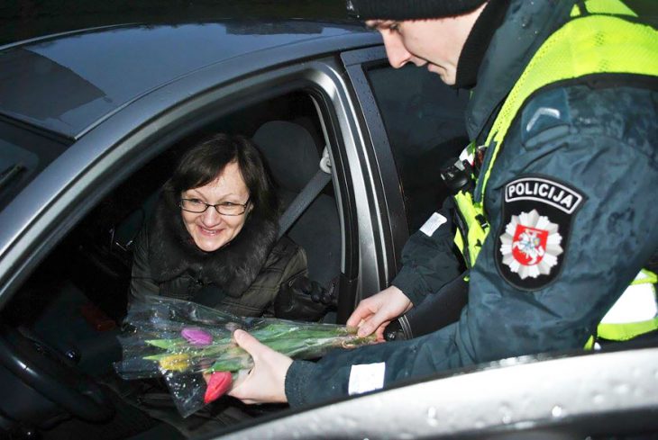 Policia entregando flores a una mujer que está conduciendo 