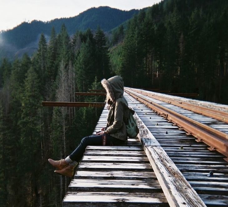 chica con abrigo en un puente sobre las montañas 