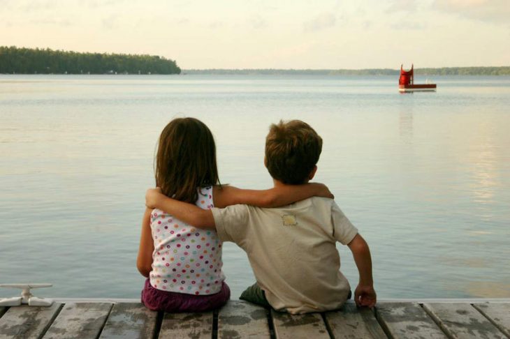 niño y niña abrazados en un muelle de espaldas