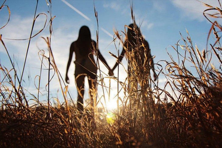 amigas agarradas de la mano de espaldas con puesta sol 