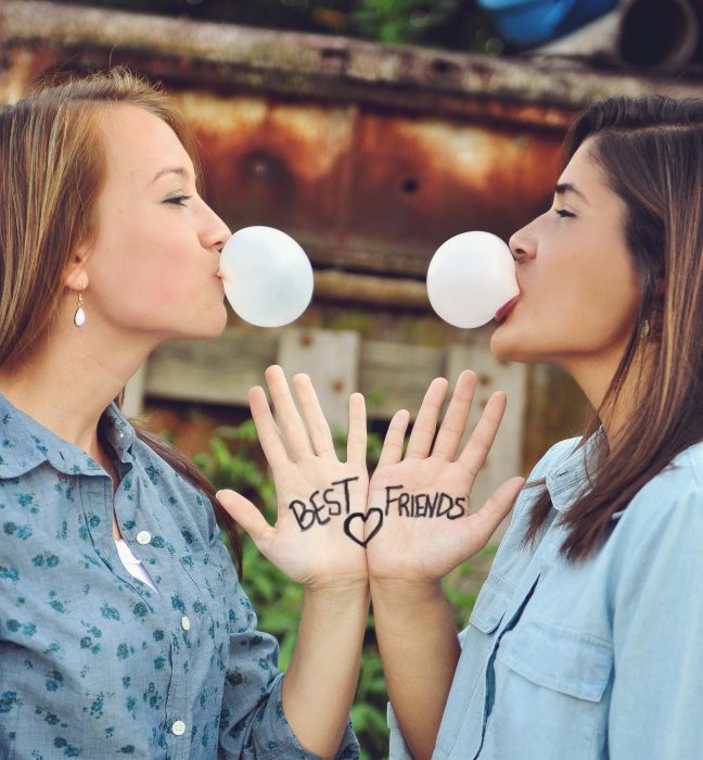 dos mujeres juntan sus manos y hacen bomba de chicle 