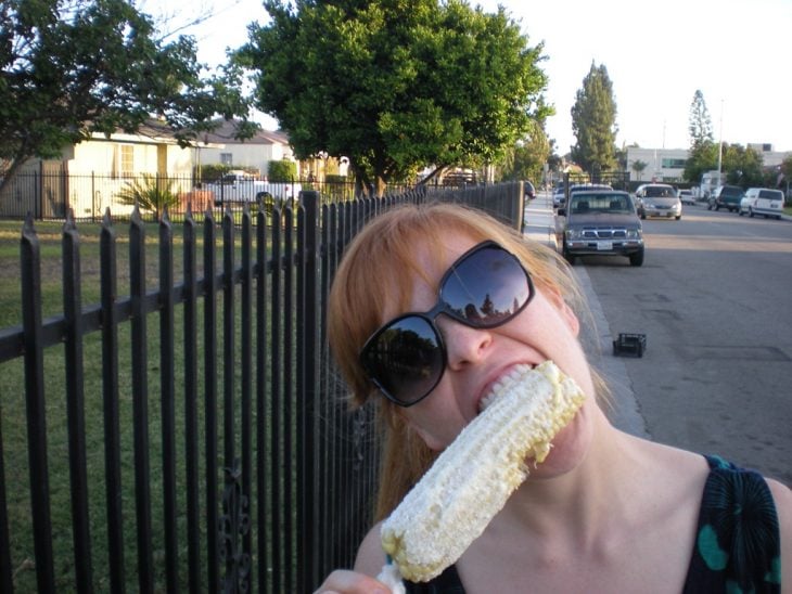 mujer feliz comiendo un elote y lentes