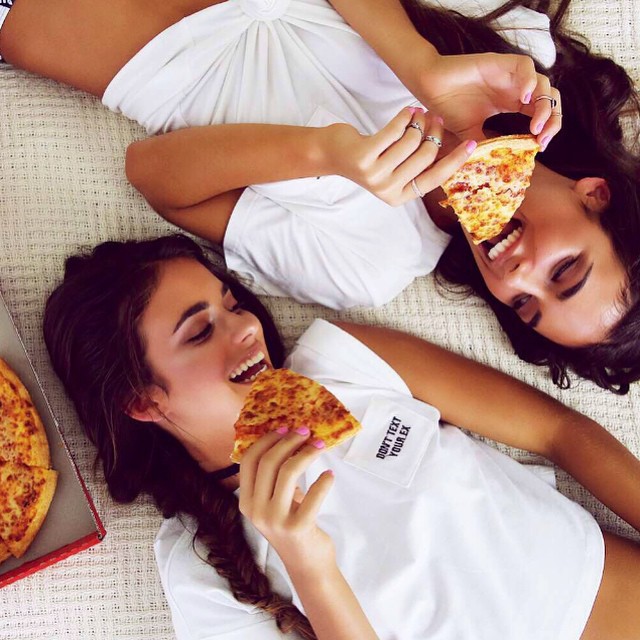 mujeres acostadas comiendo pizza sonríen 