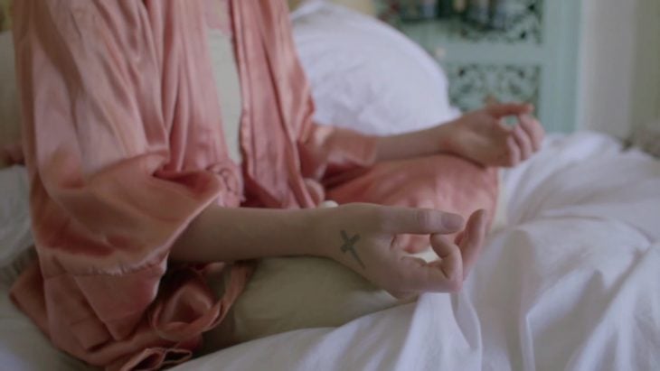 mujer sentada haciendo meditacion tatuaje de cruz 