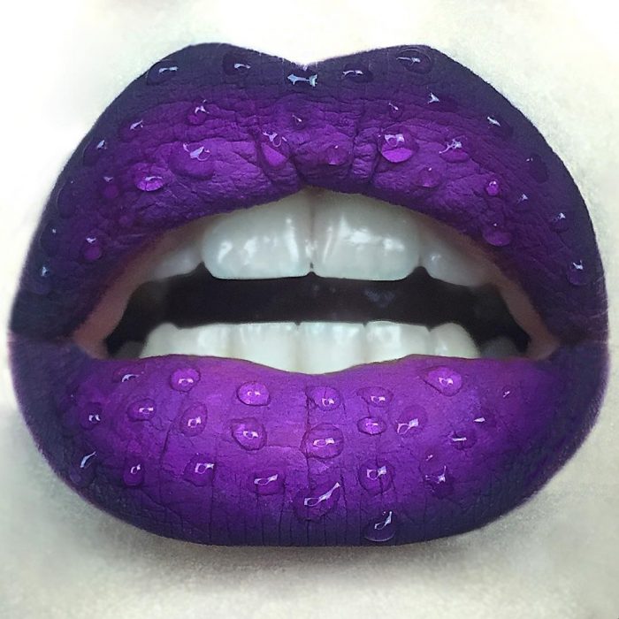 Labios pintados en color morado intenso con unos toques de gotas