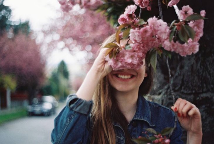 chica sonrie detras de flores rosas