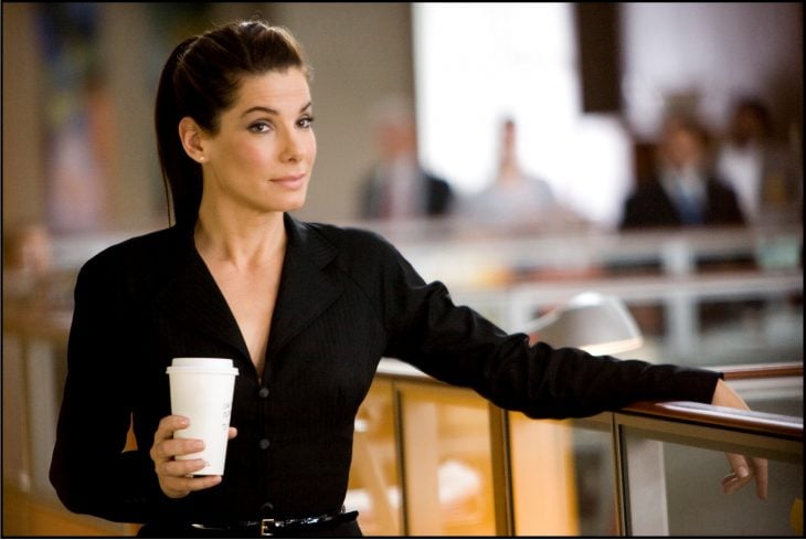 Escena de la película la propuesta chica con un café mirando intensamente a las personas 
