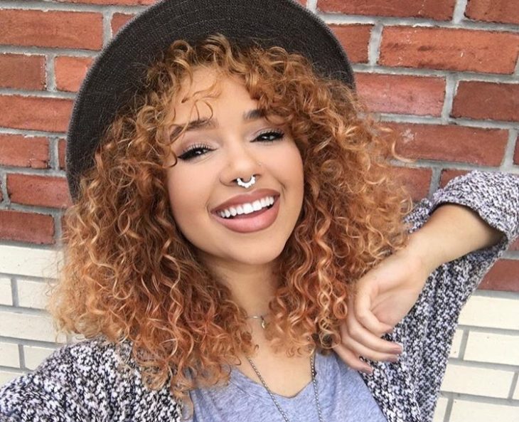 chica de cabello rizado y sombrero sonrie 