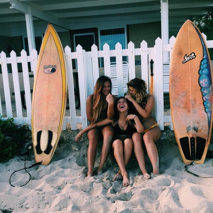 tres mujeres sentadas con tablas de surf riendo amigas 