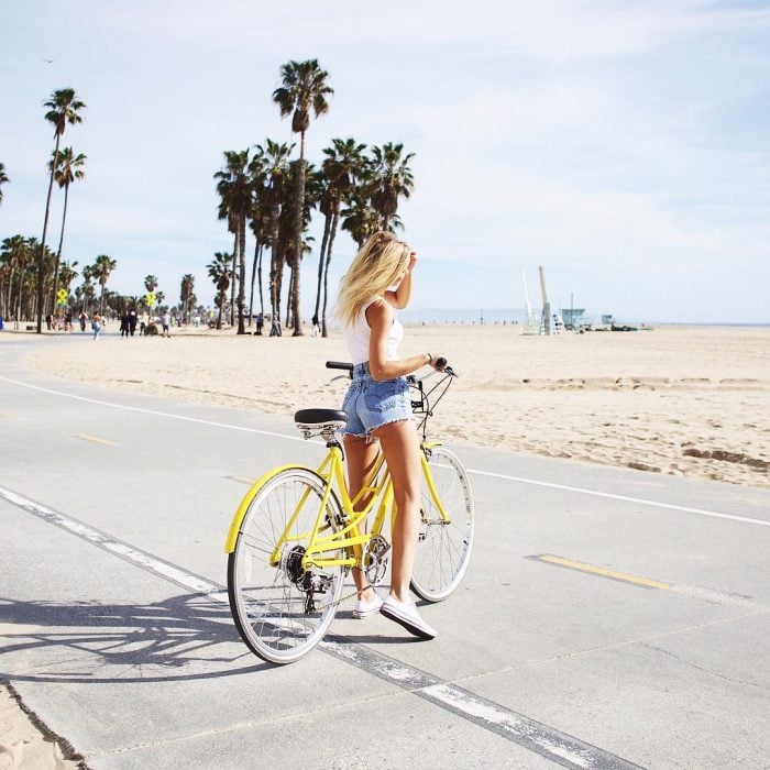 mujer rubia de cabello largo en bicicleta por la playa 