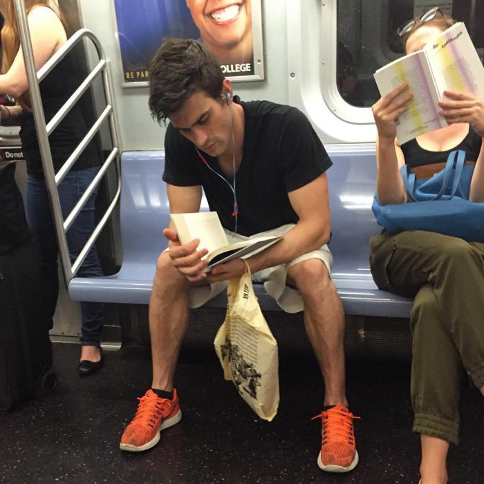 hombre sentado de playera blanca leyendo un libro 