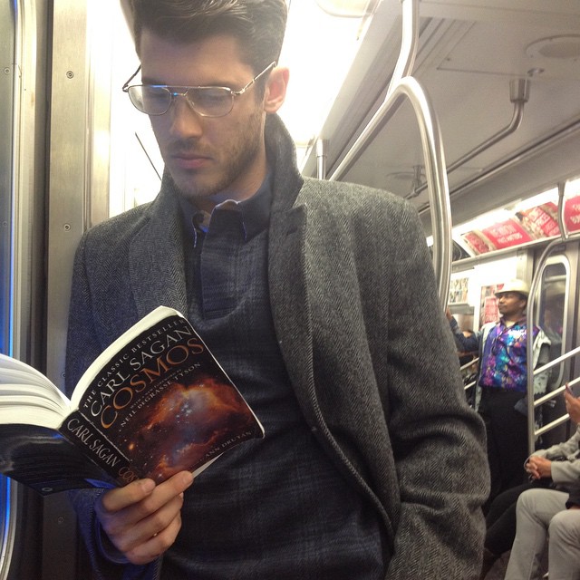 hombre de lentes de pie leyendo un libro 