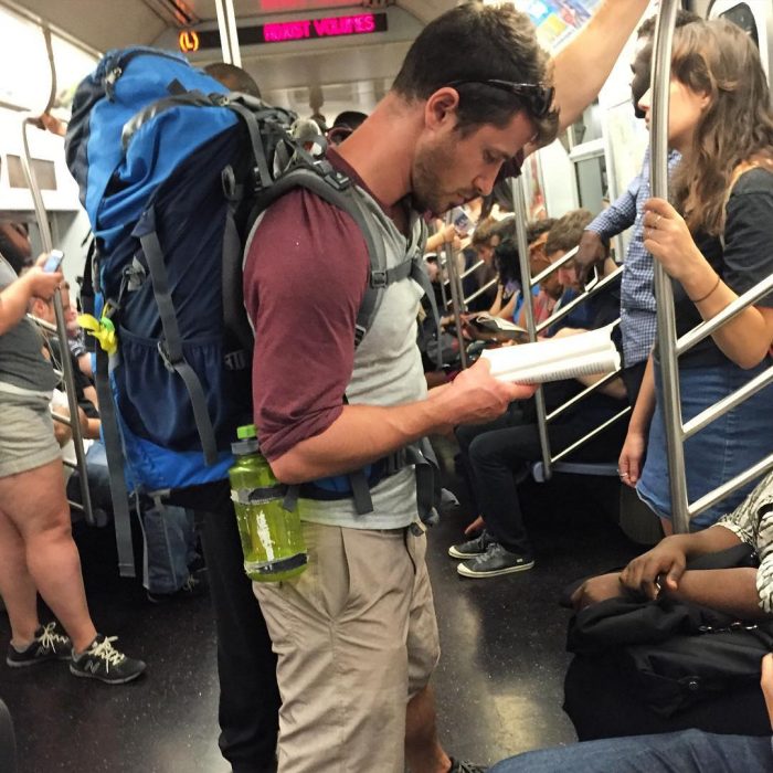 hombre con mochila azul leyendo un libro 