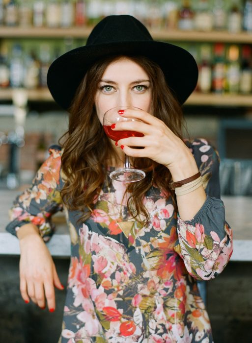 Chica recargada en la barra de un bar bebiendo vino