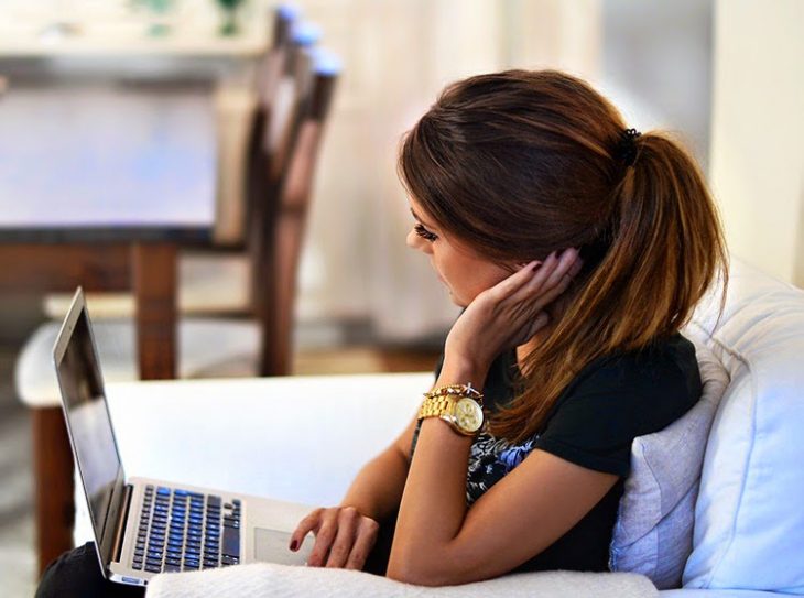 Chica sentada en un sofá revisando su computadora 