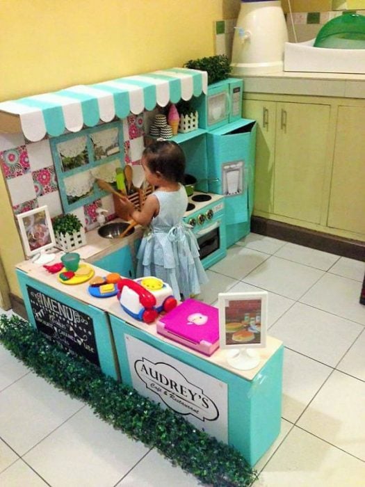 Pequeña niña jugando en una cocina hecha de cartón 